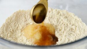 Olive oil and applesauce are being poured into a bowl of chickpea flour and dry ingredients