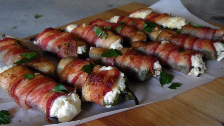 Cooked bacon-wrapped jalapeños filled with creamy cheese are served on parchment paper and garnished with fresh parsley