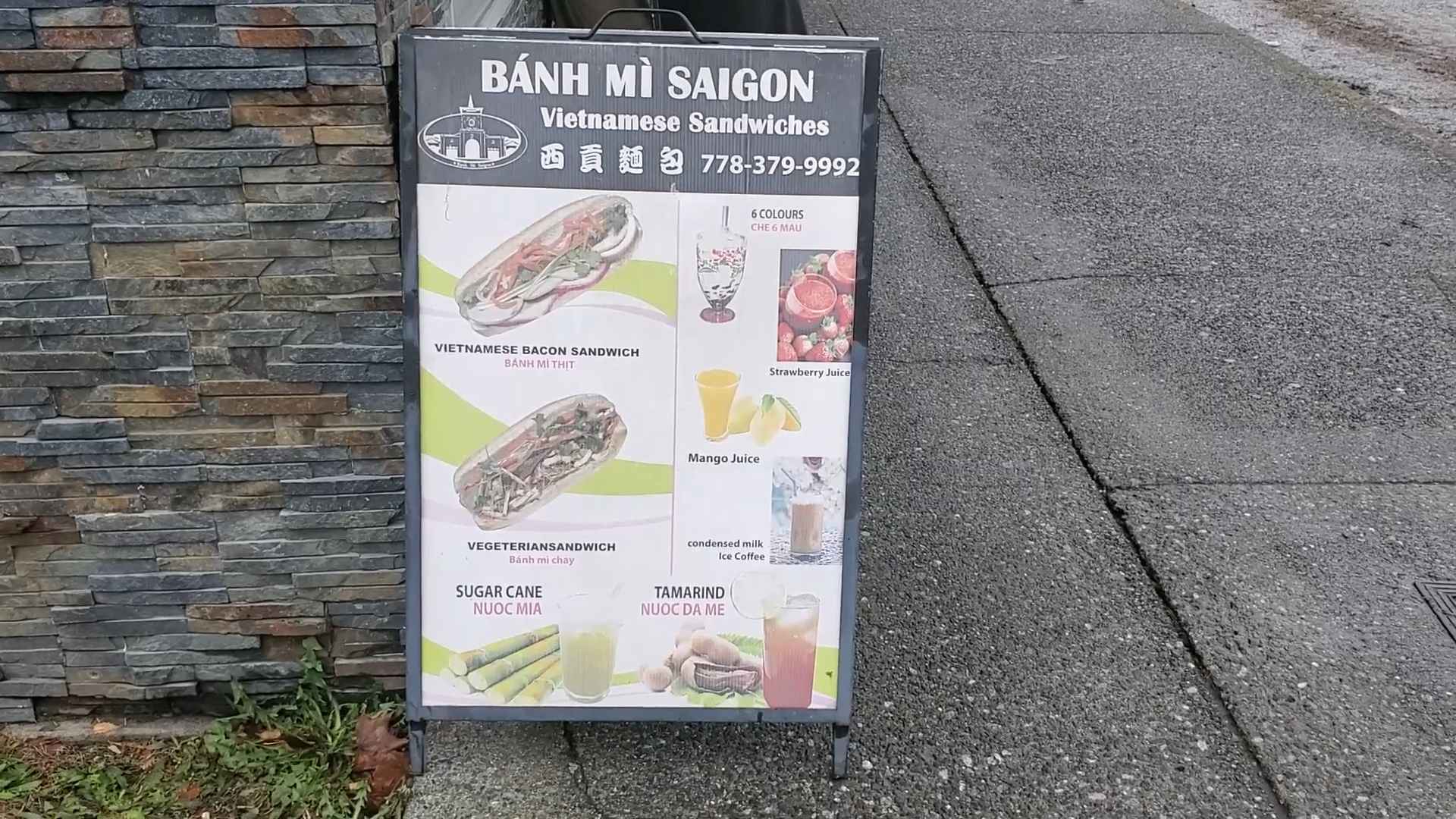 Sidewalk sign for Bánh Mì Saigon showing Vietnamese sandwiches, juices, sugar cane drink, and iced coffee