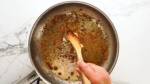 Minced garlic being stirred into a pan with browned bits and oil after searing chicken