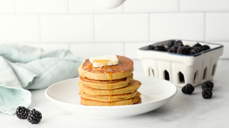 A stack of golden chickpea flour pancakes topped with butter and syrup, served with fresh blackberries on the side