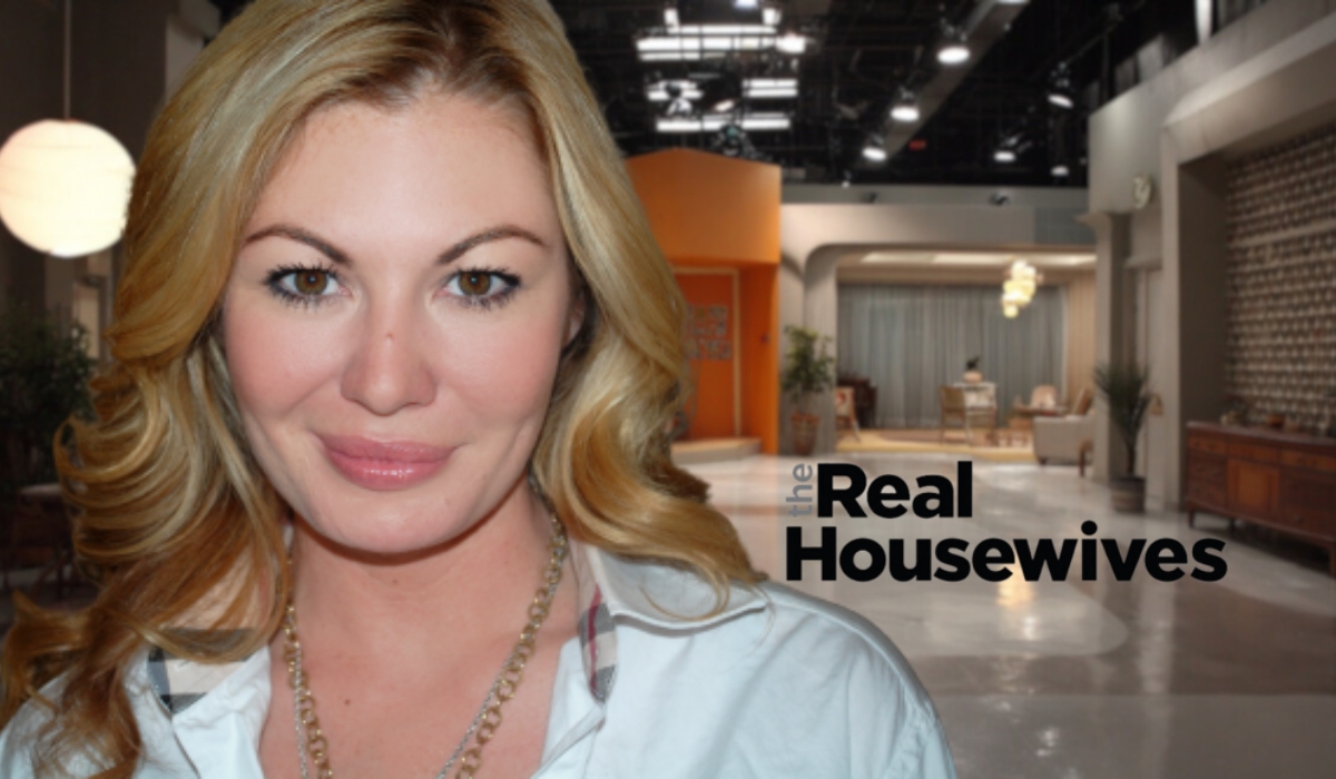 Woman with blonde hair wearing a white blouse, posing in front of a studio backdrop with The Real Housewives logo