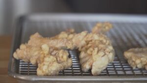 Battered chicken pieces rest on a wire rack over a baking sheet