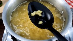 Elbow macaroni is being checked for doneness with a black spoon over a pot of boiling water