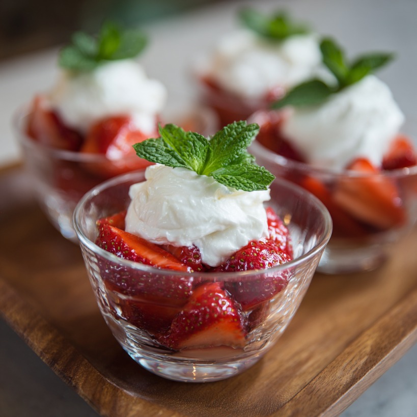 Glass cups filled with strawberries, cream, and mint leaves on a wooden tray