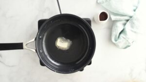 A slice of butter melts in a black nonstick skillet set over a stovetop, ready for cooking