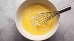 A mixing bowl with whisked wet ingredients for corn pudding, with a metal whisk resting inside