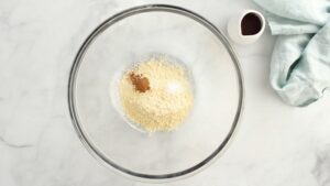 Chickpea flour, baking powder, salt, and spices are added to a clear mixing bowl, ready to be whisked together