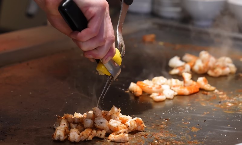A person is skillfully cutting shrimp on a grill, preparing for cooking