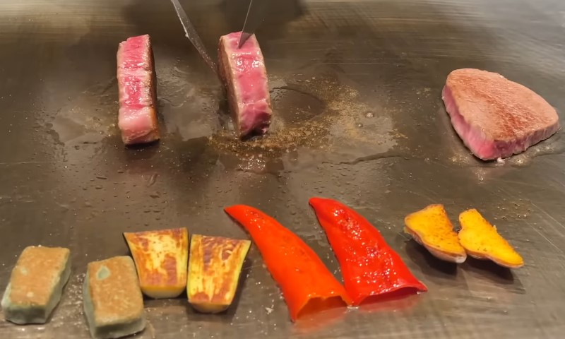 A chef skillfully grills meat on an outdoor barbecue, surrounded by a vibrant kitchen setting