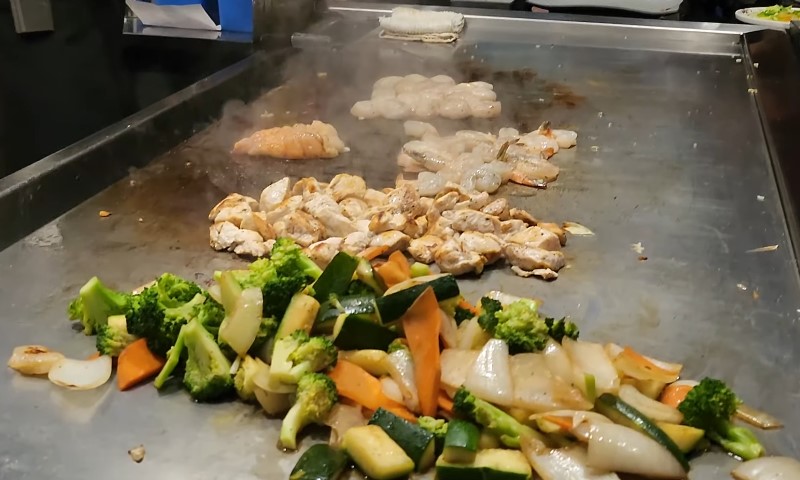 Grill filled with assorted vegetables and meat sizzling over an open flame