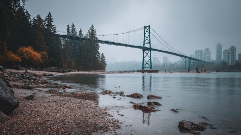 View of Lions Gate Bridge stretching over calm water with shoreline rocks and forest