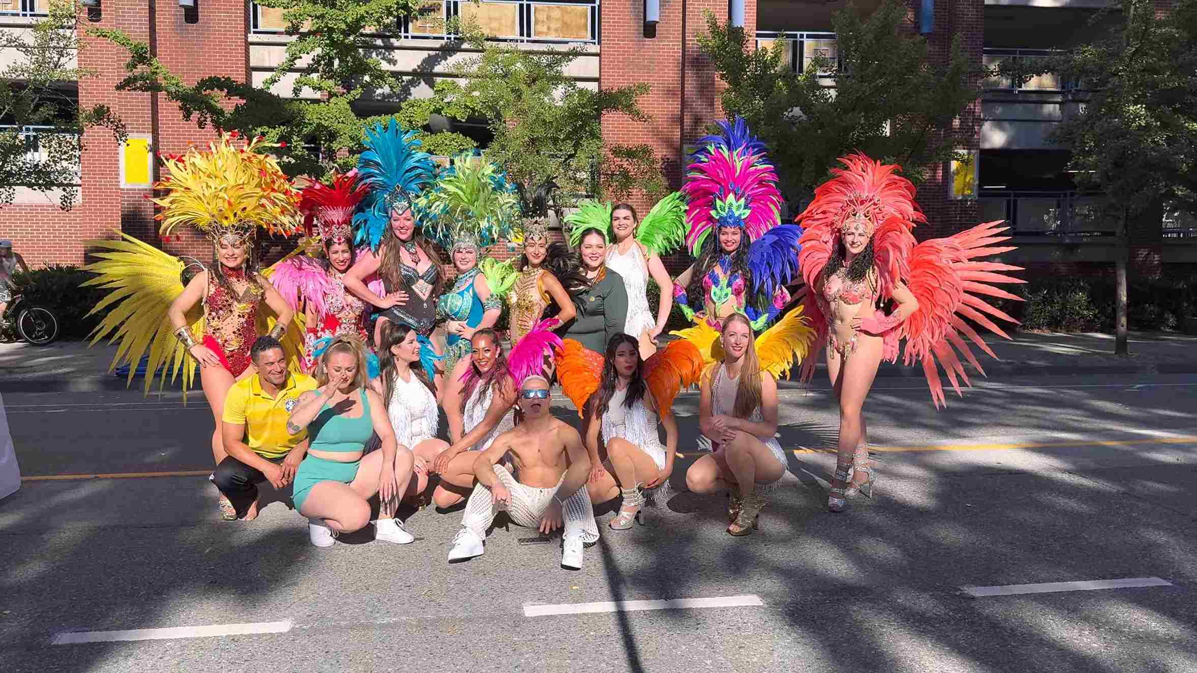 A group of performers in bright feathered costumes posing together on a city street