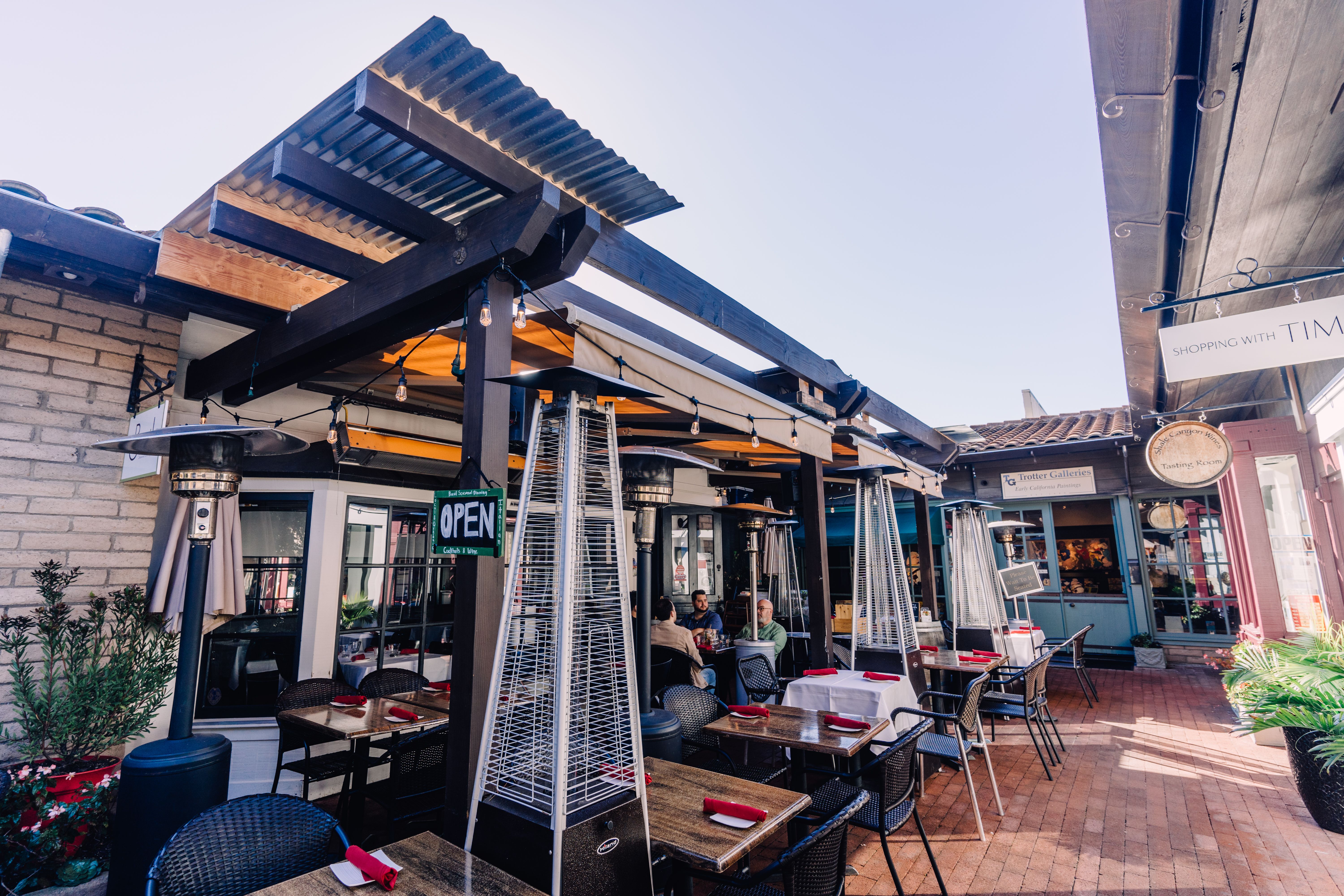 Sunny outdoor restaurant terrace with tables, chairs, and heaters under a modern pergola