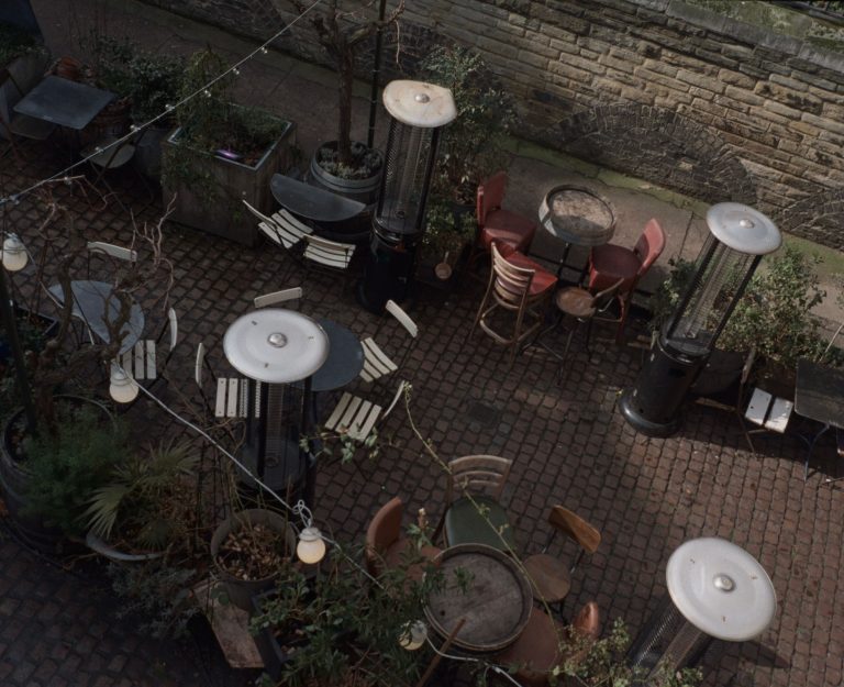 Outdoor dining area with patio heaters, tables, and chairs under ambient lighting